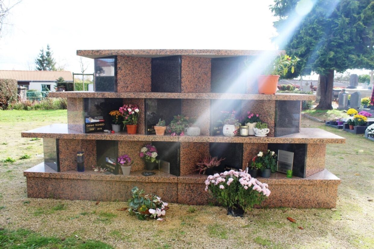 Colombarium avec fleurs dans le cimetière de Bouaye avec un rayon de soleil traversant